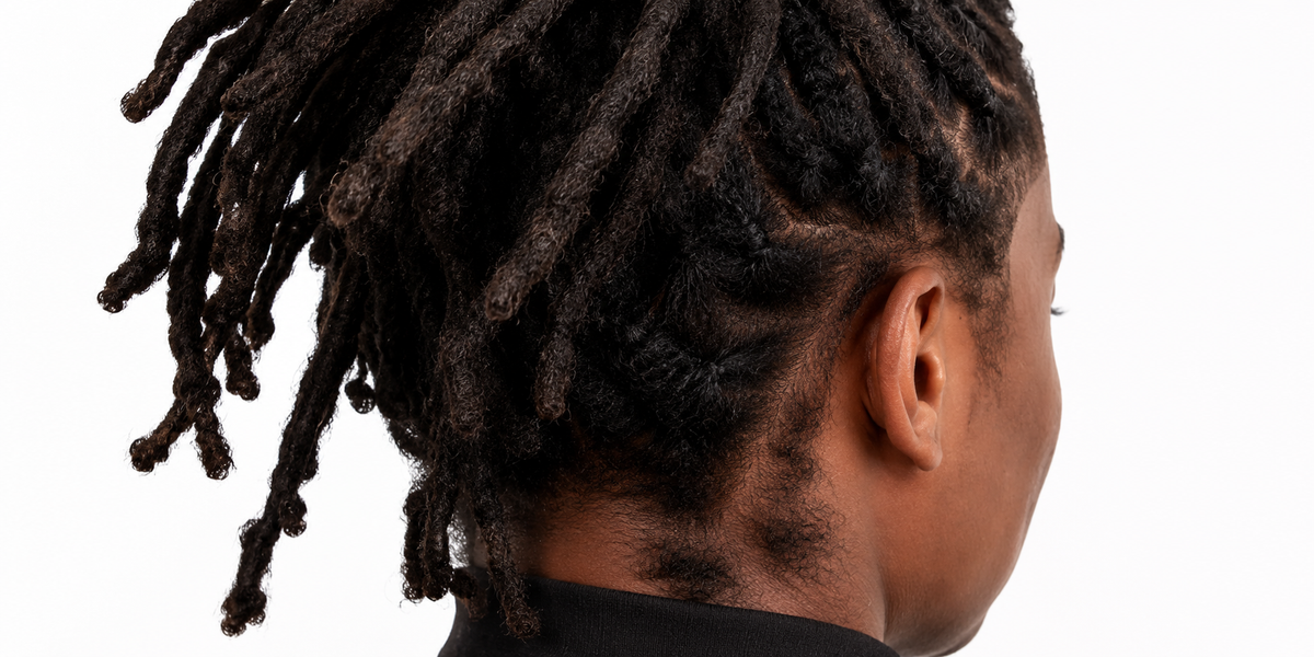 Close-up side profile of a person with dark brown to black textured dreadlocks, showing the side of the head, ear, neck, and shoulder against a plain white background.